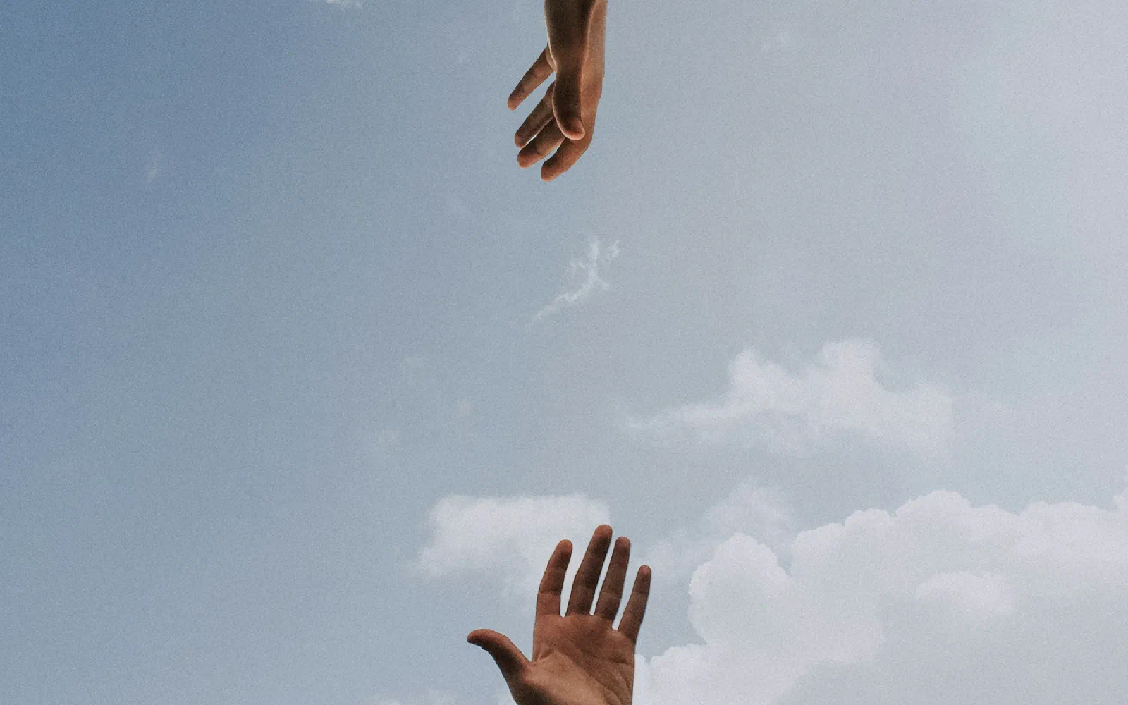Two hands reaching towards each other against a blue sky